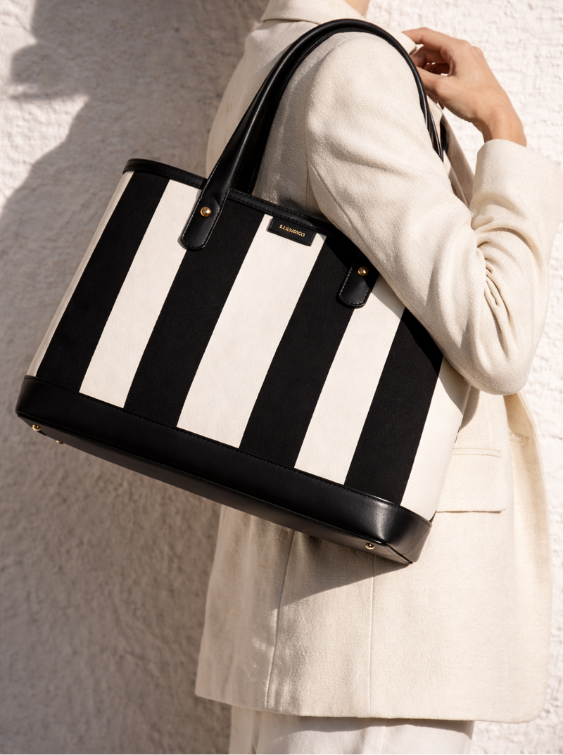 Black and white striped tote bag held by a person wearing a light-colored coat against a neutral background