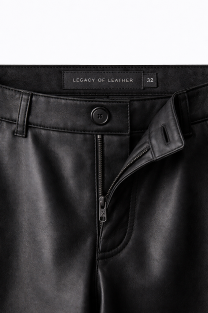 Close-up of black leather pants with a visible brand label on a white background