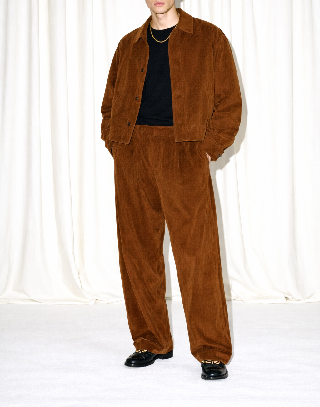 Man wearing a brown suede outfit against a white curtain background